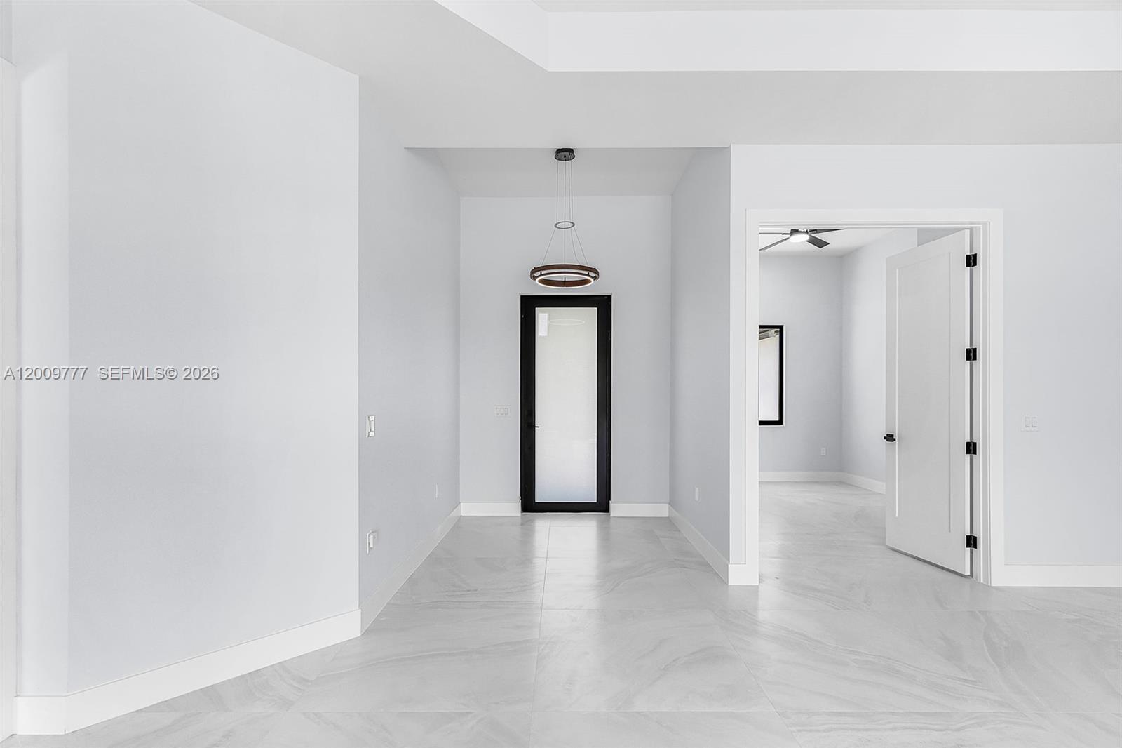 A bright, minimalist hallway with white walls, light tile flooring, and a modern pendant light — 2303 NW 35 AVE, Cape Coral FL 33993, CAPE CORAL, FL