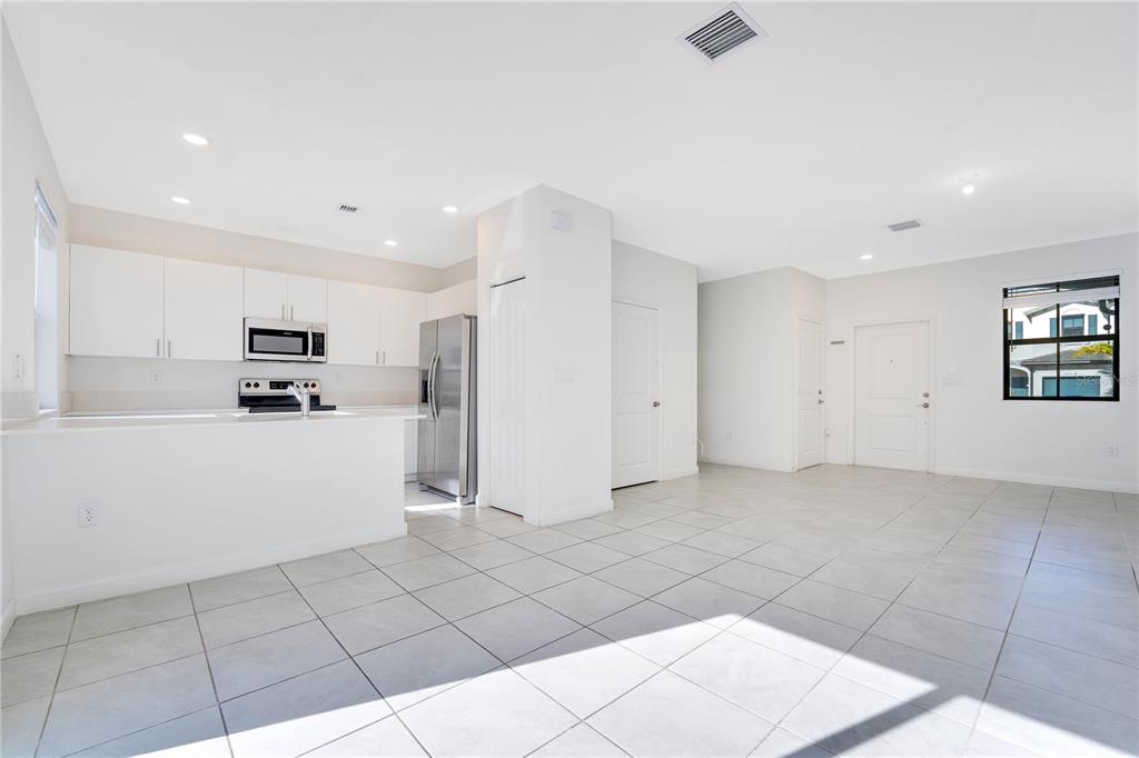 A bright, open-concept kitchen and living area featuring white cabinetry, stainless appliances, and tiled floors — 28517 SW 134TH AVENUE, HOMESTEAD, FL