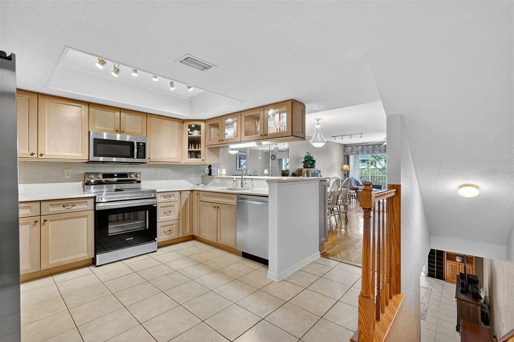 A kitchen with light wood cabinets, stainless steel appliances, and tile flooring overlooks a dining area — 14879 SEMINOLE TRAIL, SEMINOLE, FL