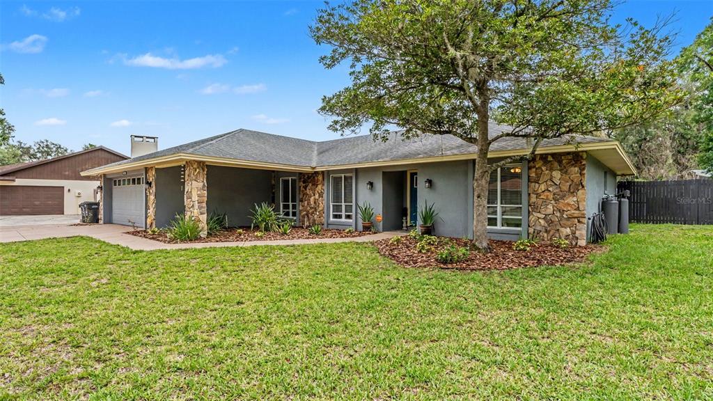 A single-story gray house with stone accents and a large tree in the front yard — 5776 DEER FLAG DRIVE, LAKELAND, FL