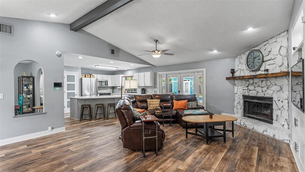 An open-concept living room features a stone fireplace, leather sectional, and adjacent kitchen with island — 5776 DEER FLAG DRIVE, LAKELAND, FL