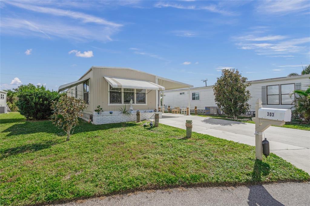 A beige manufactured home features a white brick base, a carport, and a mailbox — 303 MARLETTE DRIVE, NORTH PORT, FL