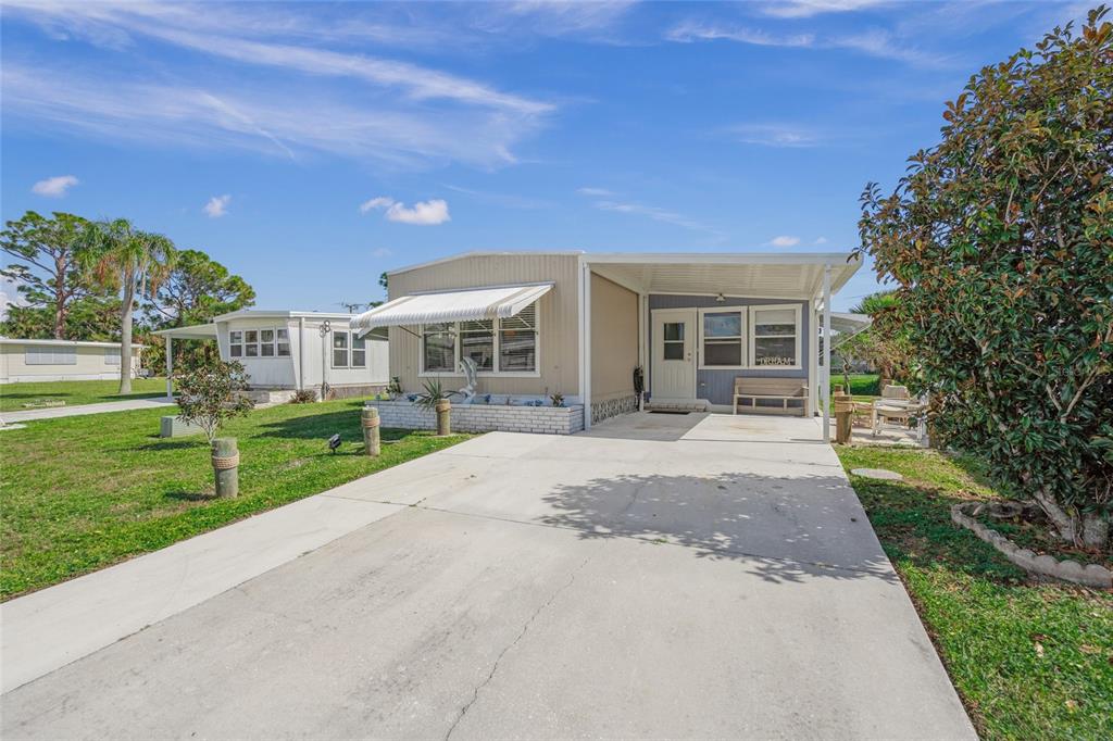 A single-story mobile home with a concrete driveway, carport, and white awning under a blue sky — 303 MARLETTE DRIVE, NORTH PORT, FL