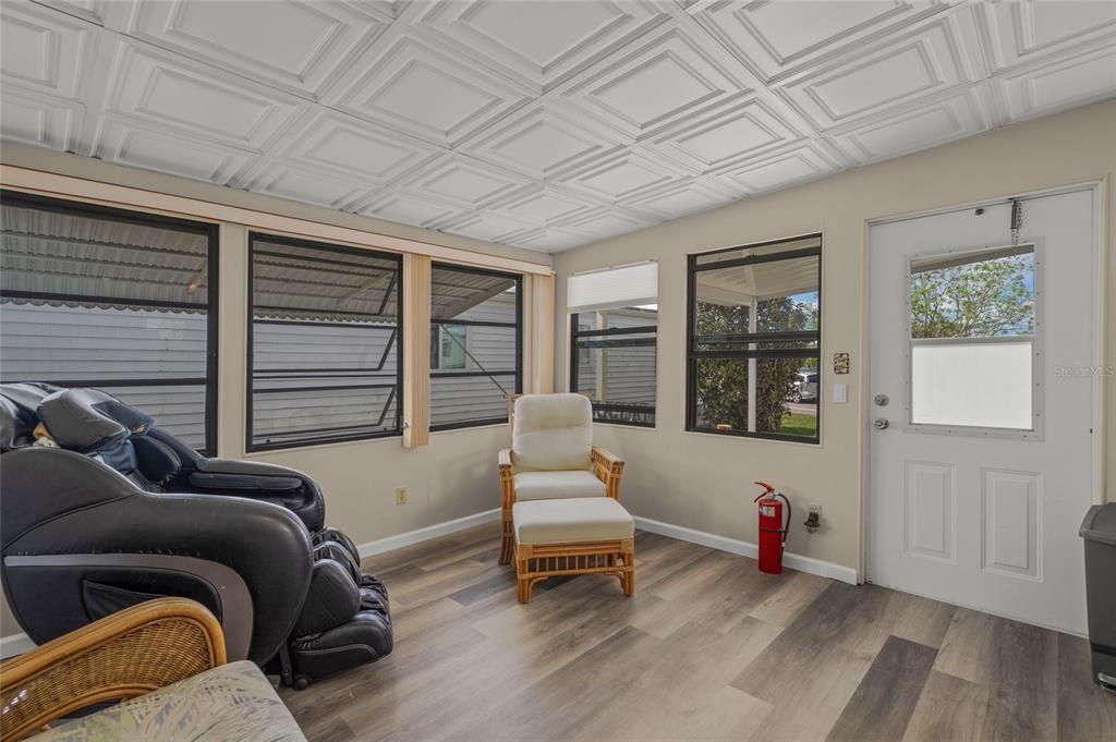 A sunroom features a coffered ceiling, wood-look flooring, a massage chair, and a wicker chair — 303 MARLETTE DRIVE, NORTH PORT, FL
