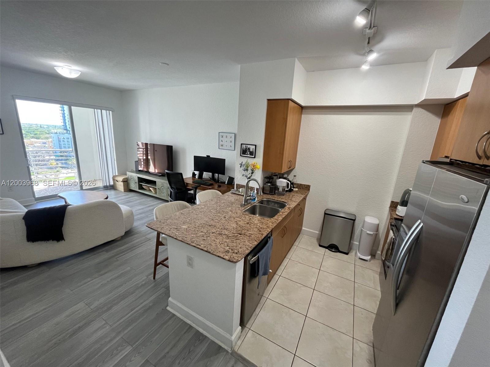 An open-concept kitchen with granite countertops overlooks a living area with a balcony view — 1830 Radius Dr # 1218, Hollywood FL 33020, HOLLYWOOD, FL