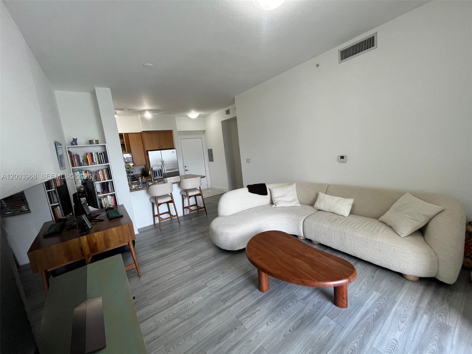 A living room features a curved sofa, a wooden coffee table, and an adjacent kitchen area — 1830 Radius Dr # 1218, Hollywood FL 33020, HOLLYWOOD, FL