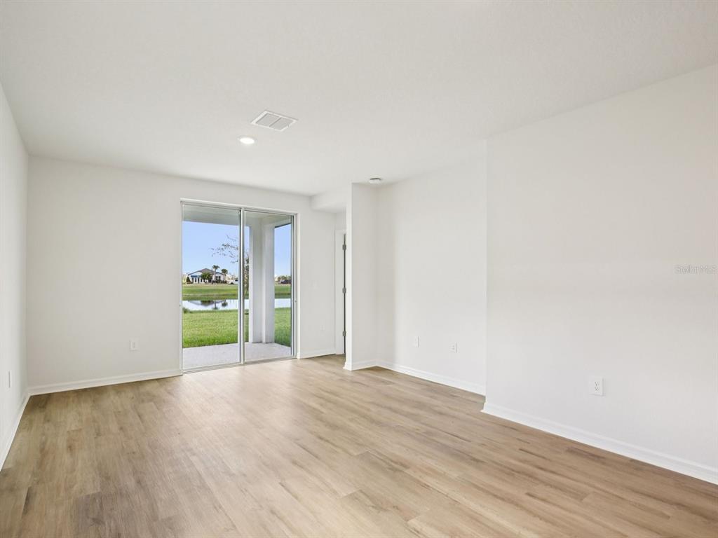 An empty room with light wood-look flooring, white walls, and a sliding glass door — 161 CANOE BEND AVENUE, NOKOMIS, FL