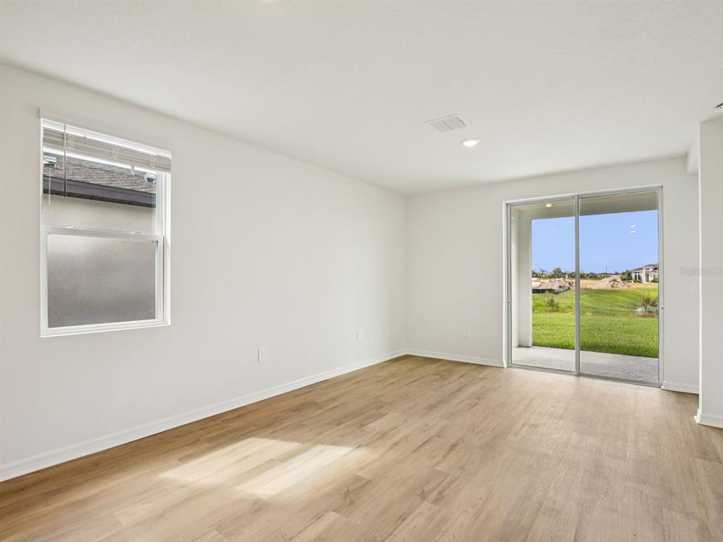 An empty room with light wood-look flooring, white walls, a window, and sliding glass doors — 161 CANOE BEND AVENUE, NOKOMIS, FL