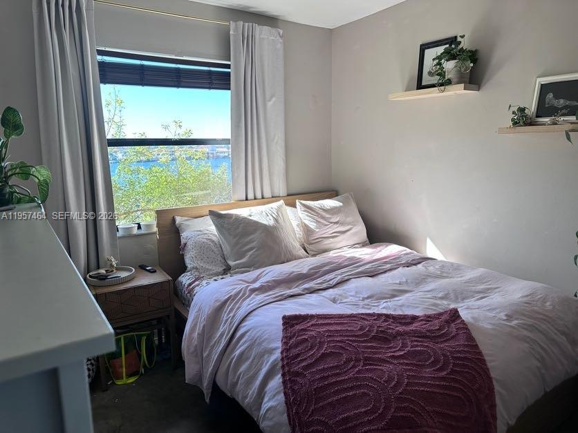 A bedroom features a bed with a pink throw, a window with water views, and shelves — 2480 W 67th Pl # 12, Hialeah FL 33016, HIALEAH, FL