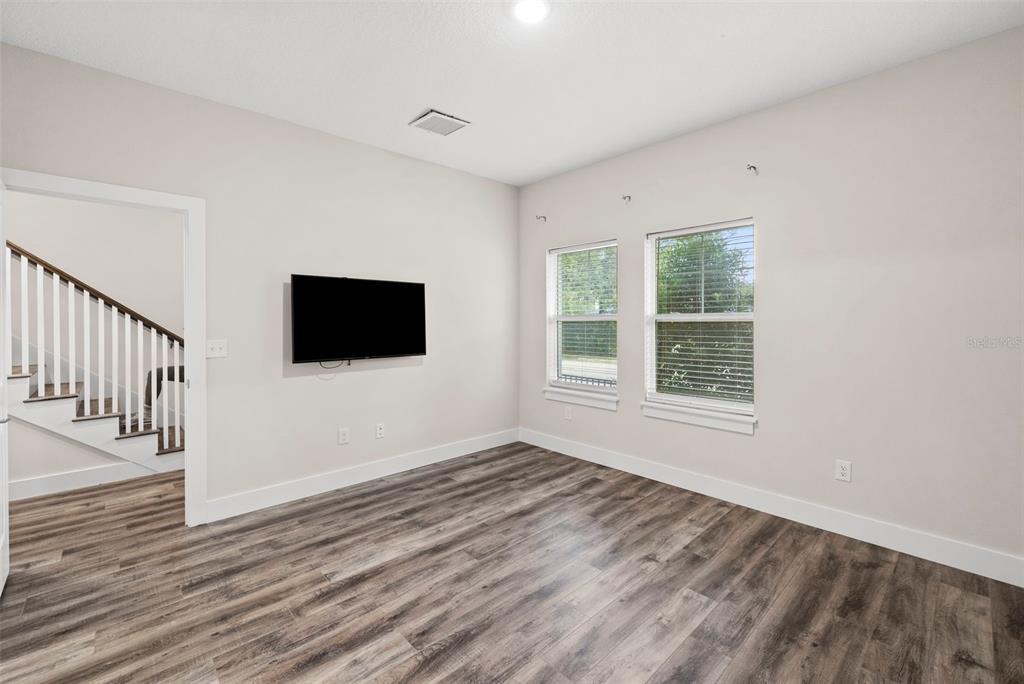 A room with light-colored walls, wood-look flooring, two windows, and a wall-mounted television — 3122 W AZEELE STREET UNIT 3, TAMPA, FL