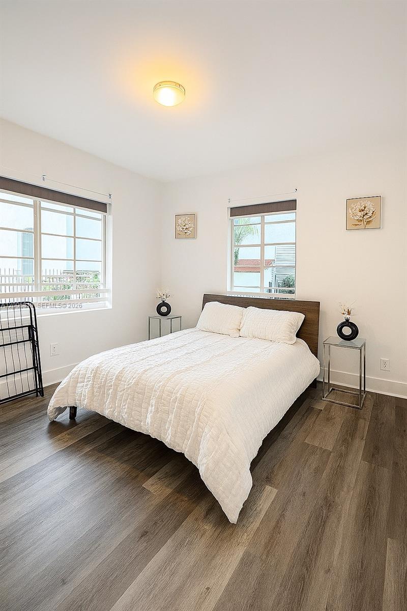 A bedroom features a bed with a wooden headboard, two windows, and wood-look flooring — 600 15th St # 4, Miami Beach FL 33139, MIAMI BEACH, FL