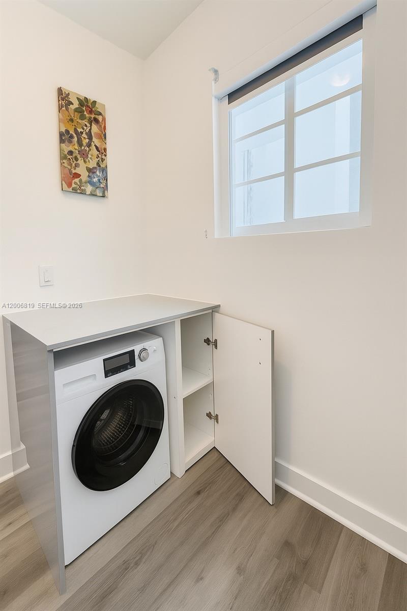A laundry room features a front-loading washing machine, white cabinetry, and a window — 600 15th St # 4, Miami Beach FL 33139, MIAMI BEACH, FL