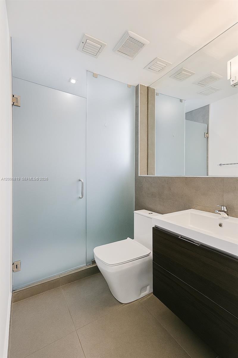 A modern bathroom features a frosted glass shower, a white toilet, and a dark vanity — 600 15th St # 4, Miami Beach FL 33139, MIAMI BEACH, FL