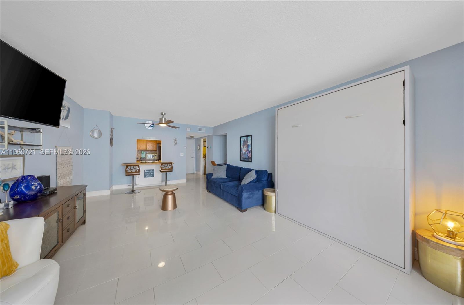 A living room features light blue walls, white tile floors, a blue sofa, and a murphy bed — 3180 S Ocean Dr # 607, Hallandale Beach FL 33009, HALLANDALE BEACH, FL