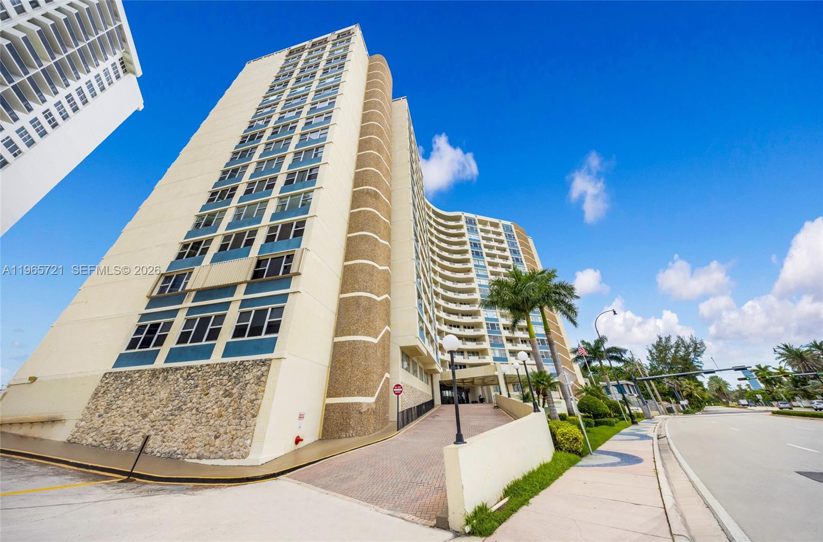 A low-angle exterior view of a tall, curved apartment building with a paved entrance ramp — 3180 S Ocean Dr # 607, Hallandale Beach FL 33009, HALLANDALE BEACH, FL