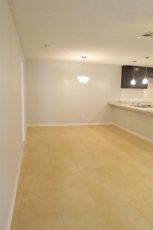 An open dining area with light-colored tile flooring, a hanging light fixture, and a kitchen counter — 1513 SOPHIE BOULEVARD, ORLANDO, FL