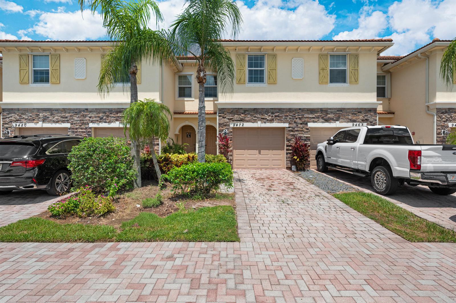 A row of two-story townhouses features stone-veneer lower levels, beige stucco upper walls, and driveways — 9472 SW Merlin Court, Stuart FL 34997, STUART, FL