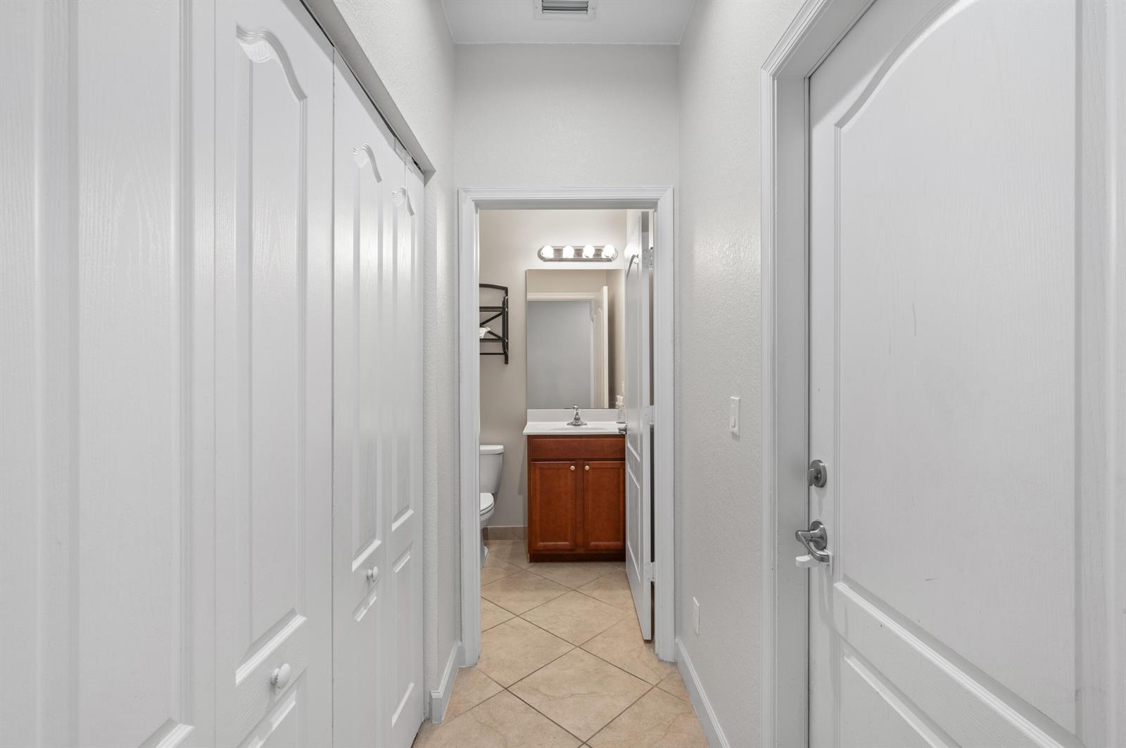 A hallway with white doors leads to a bathroom featuring a wood vanity and mirror — 9472 SW Merlin Court, Stuart FL 34997, STUART, FL