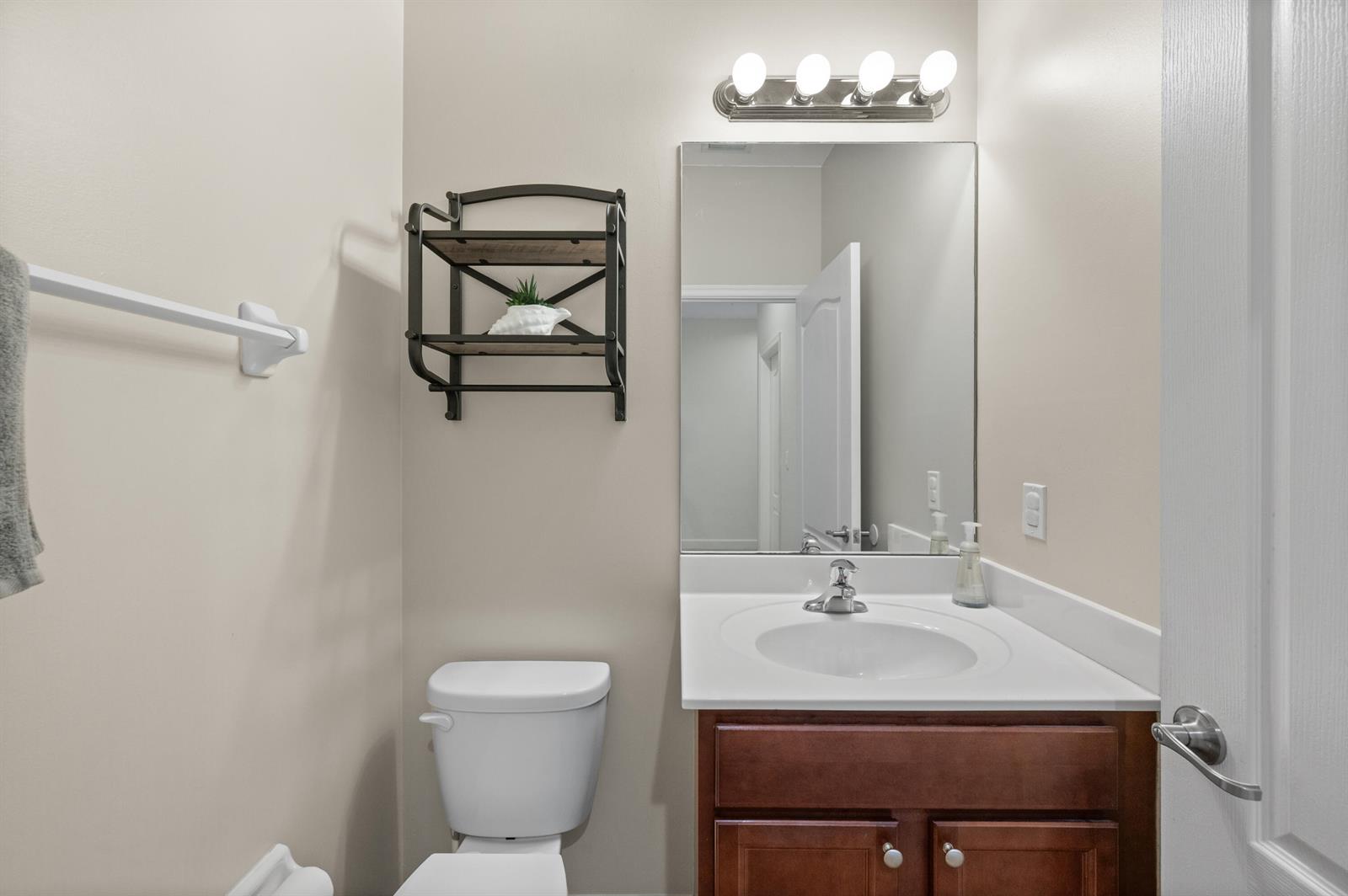 A small bathroom features a vanity with a white countertop, a mirror, and wall shelving — 9472 SW Merlin Court, Stuart FL 34997, STUART, FL
