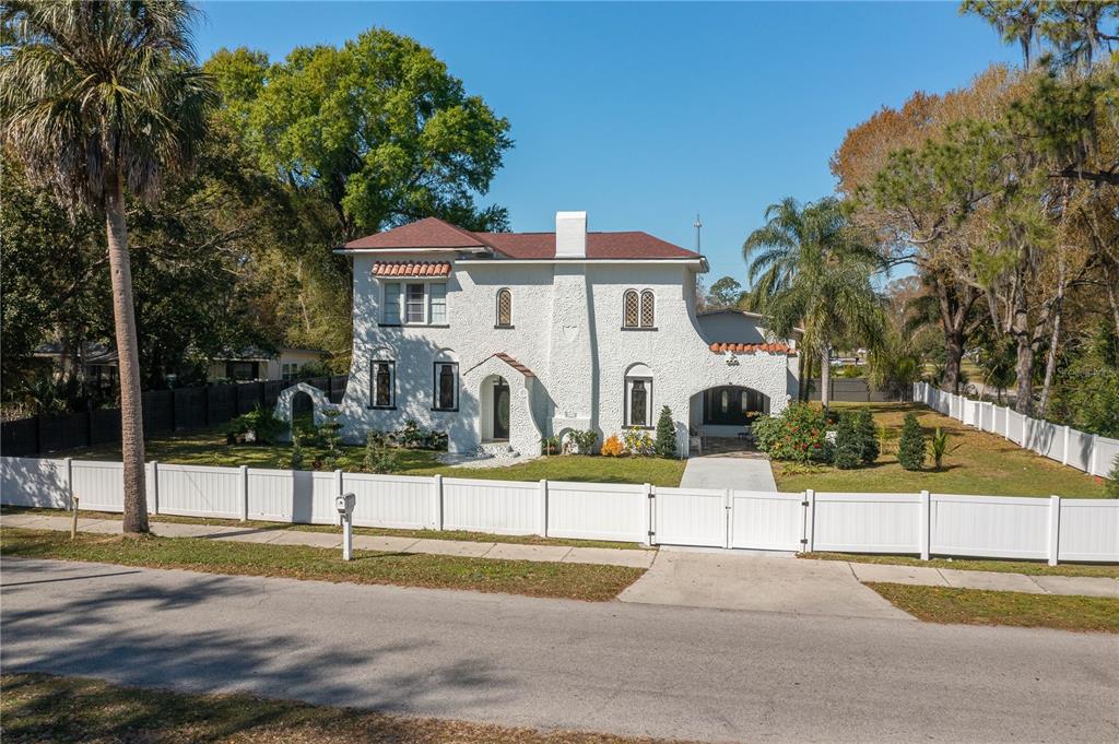 A white two-story stucco house with a red tile roof sits behind a white fence — 409 21ST STREET SW, WINTER HAVEN, FL