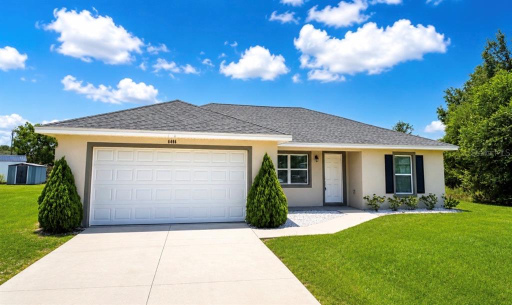 A single-story house with a two-car garage, light-colored stucco exterior, and a gray shingled roof — 6486 SW 129TH STREET, OCALA, FL