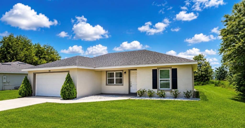 A single-story house with a beige stucco exterior, a two-car garage, and a grassy lawn — 6486 SW 129TH STREET, OCALA, FL