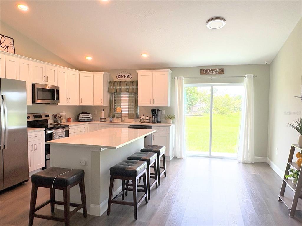 A kitchen features white cabinets, a central island with bar stools, and sliding glass doors — 6486 SW 129TH STREET, OCALA, FL