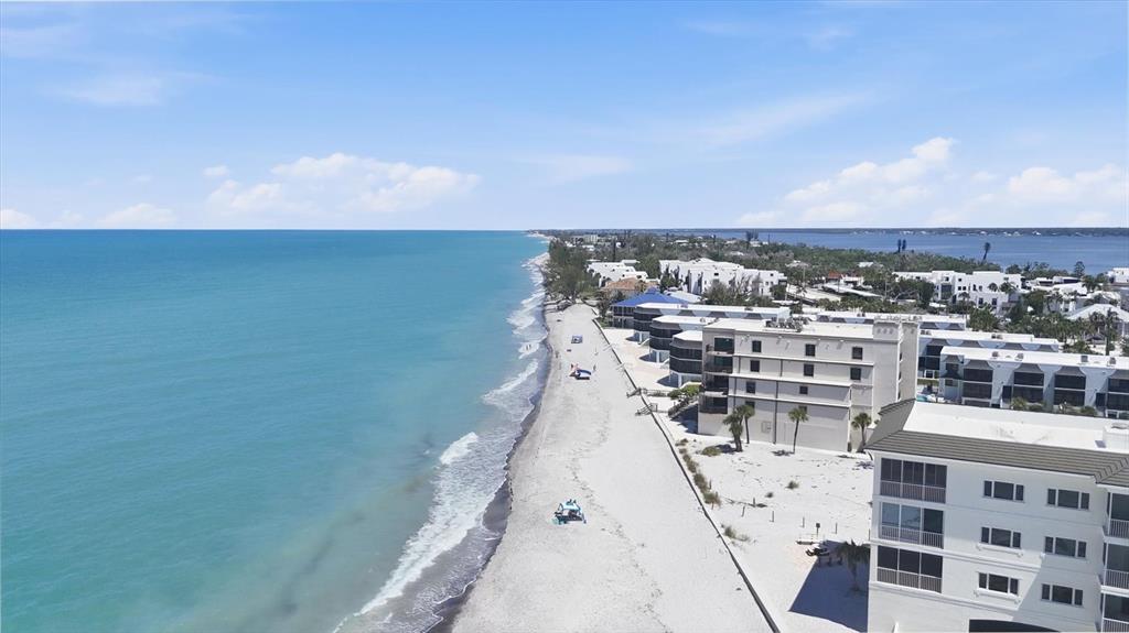 An aerial view of a sandy beach coastline with multi-story white residential buildings — 2729 N BEACH ROAD UNIT 211, ENGLEWOOD, FL