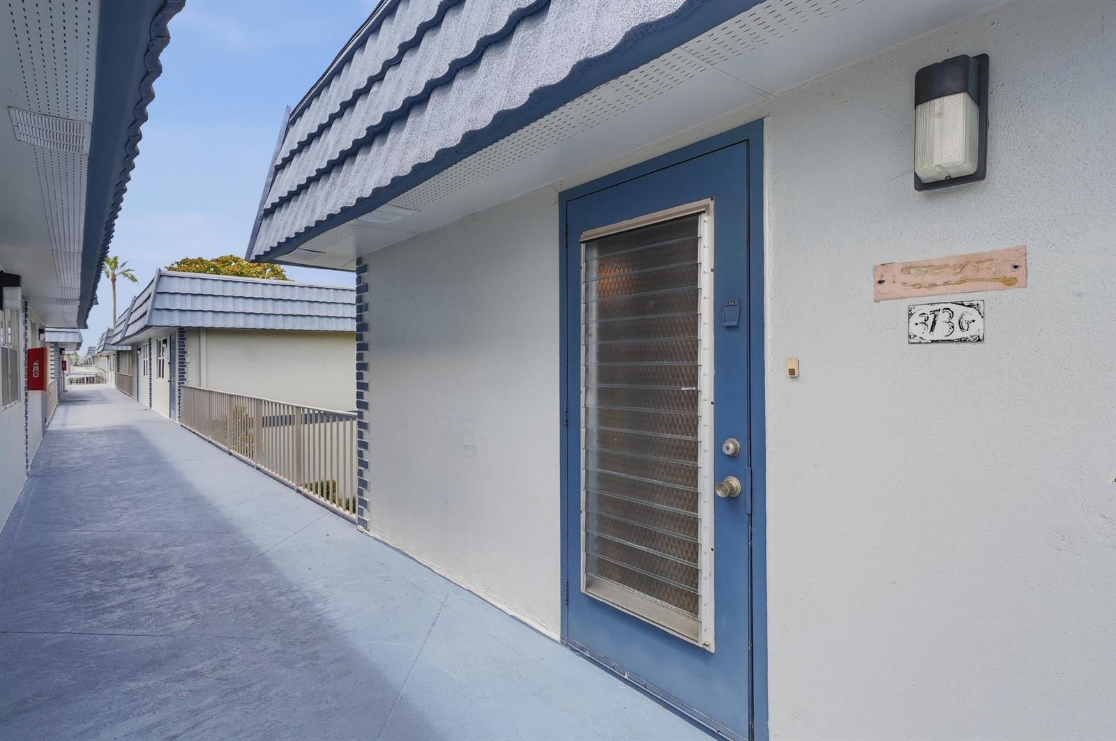 An exterior view of a blue door and walkway at a multi-story apartment complex — 373 Tuscany G, Delray Beach FL 33446, DELRAY BEACH, FL