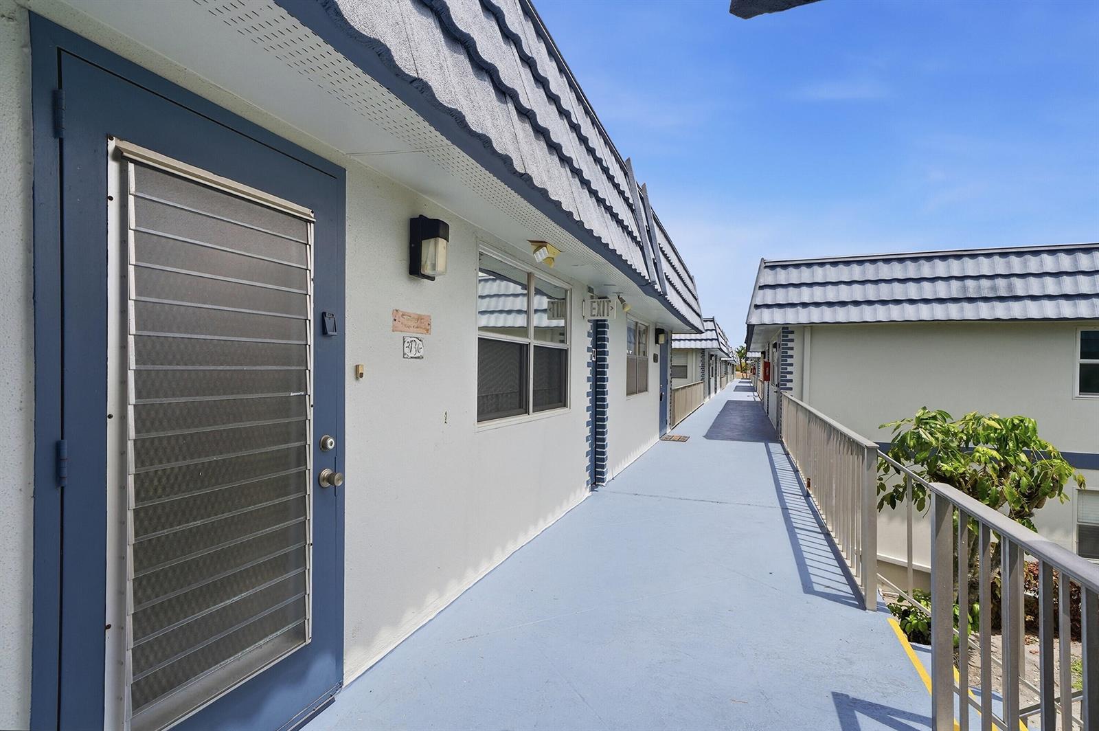 An exterior walkway leads past blue doors and windows of a multi-story apartment building — 373 Tuscany G, Delray Beach FL 33446, DELRAY BEACH, FL
