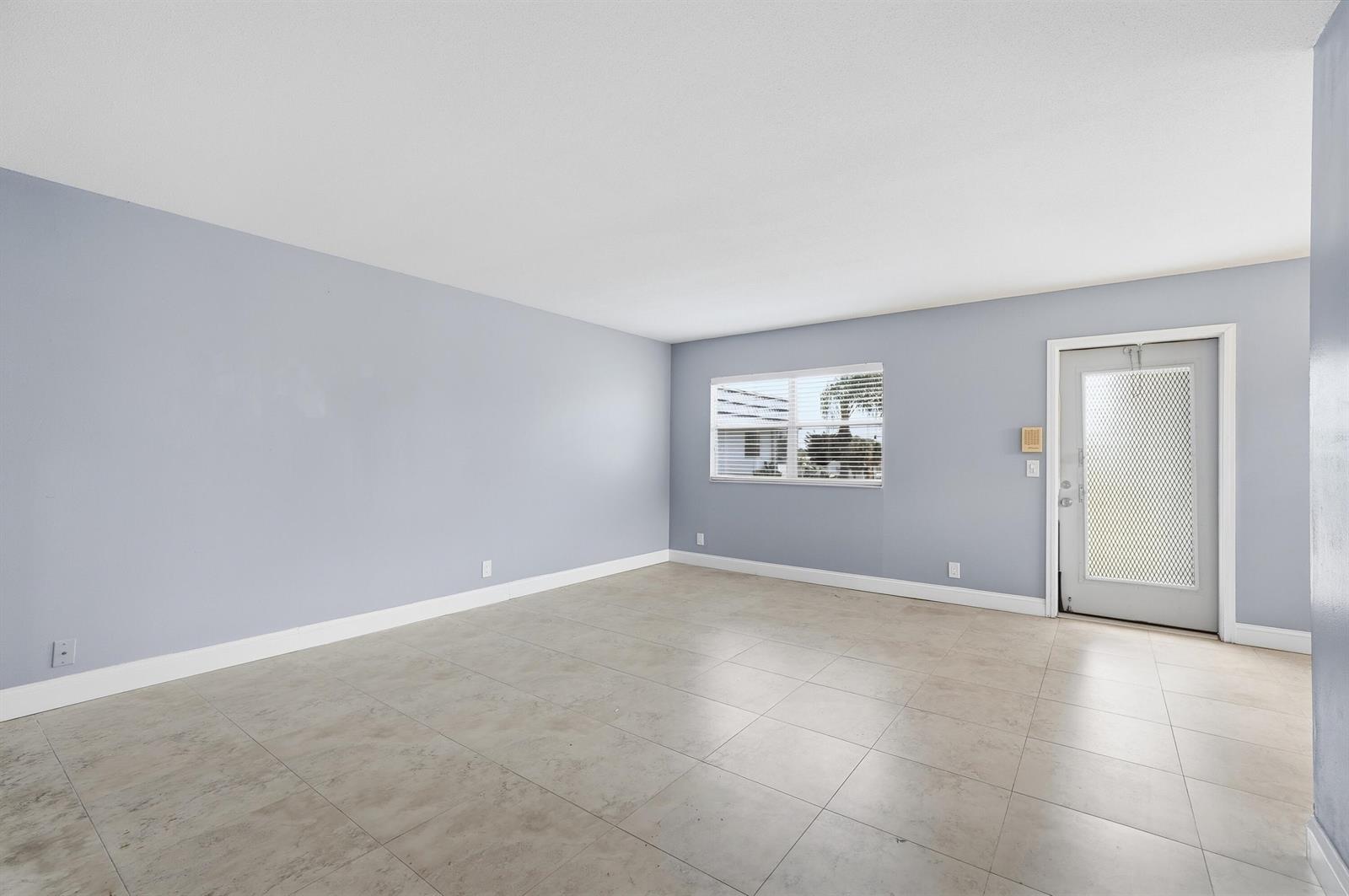 An empty room with light blue walls, large beige floor tiles, and a white door — 373 Tuscany G, Delray Beach FL 33446, DELRAY BEACH, FL