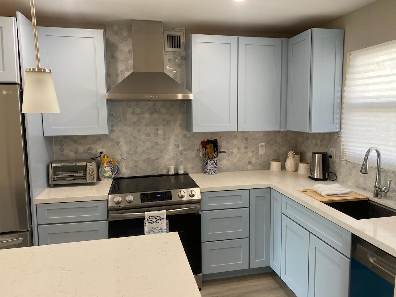 A kitchen featuring light blue cabinets, a stainless steel range hood, and a hexagonal tile backsplash — 311 E Ocean Avenue # 309, Lantana FL 33462, LANTANA, FL