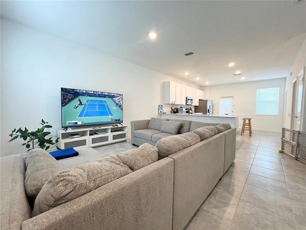 A living room with a large sectional sofa faces a television and an open kitchen — 6021 BLISSFUL STREET, CLERMONT, FL