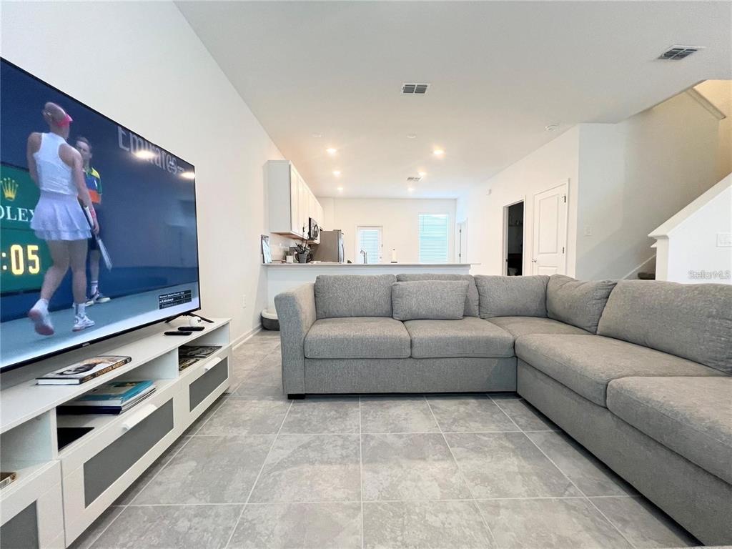 A living room features a large gray sectional sofa, a television, and tile flooring — 6021 BLISSFUL STREET, CLERMONT, FL