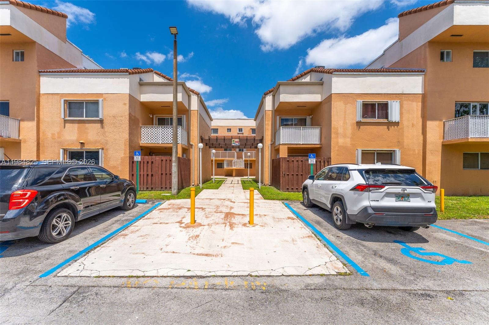 A view of a residential building exterior with two parked cars in handicap spaces — 14907 SW 80th St # 115, Miami FL 33193, MIAMI, FL