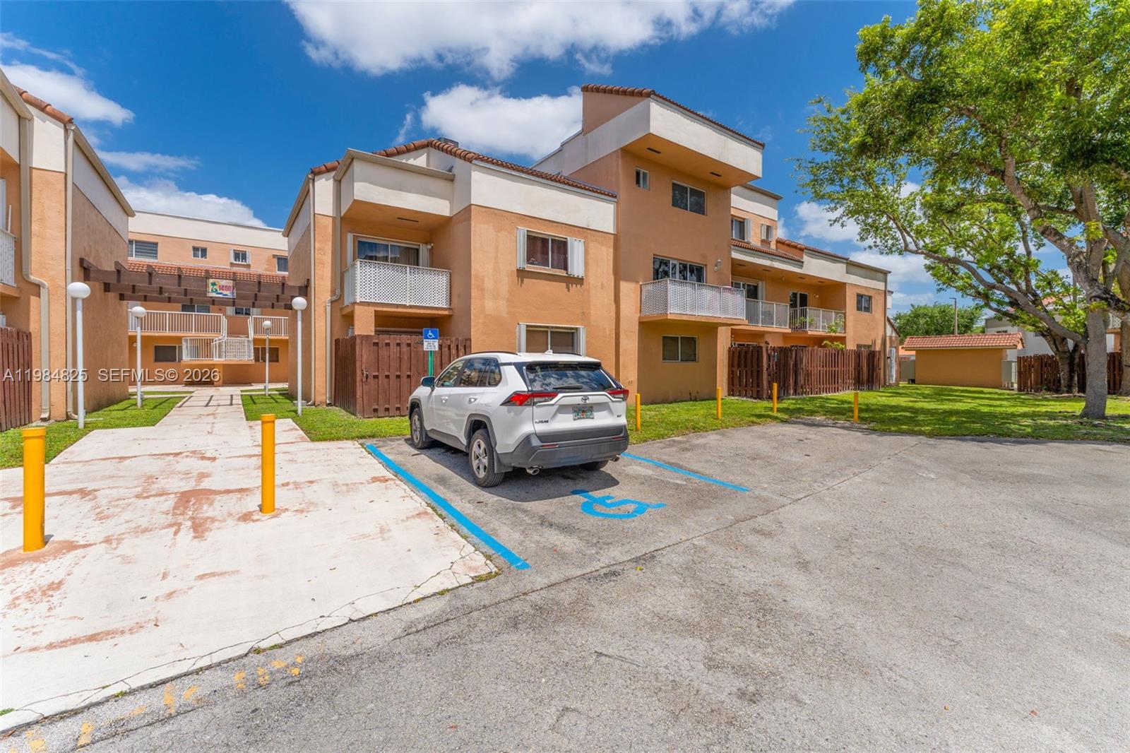 A white SUV is parked in a designated handicap spot in front of a tan apartment building — 14907 SW 80th St # 115, Miami FL 33193, MIAMI, FL