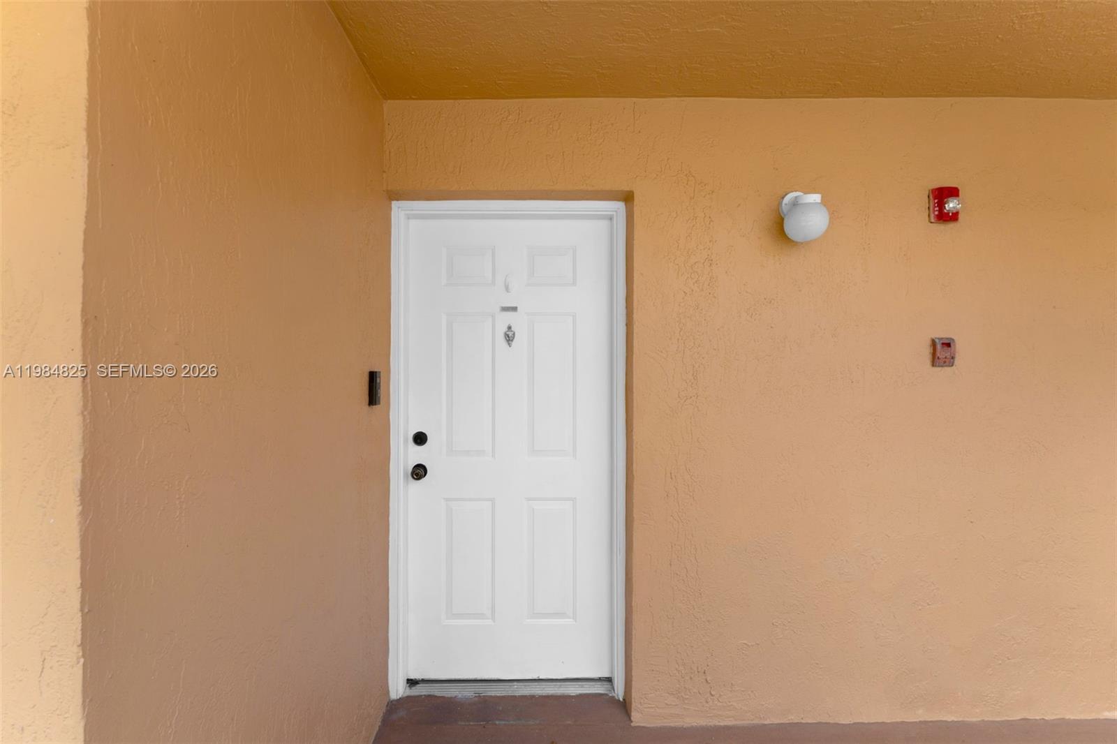 A white front door is centered on a plain, light orange exterior wall — 14907 SW 80th St # 115, Miami FL 33193, MIAMI, FL