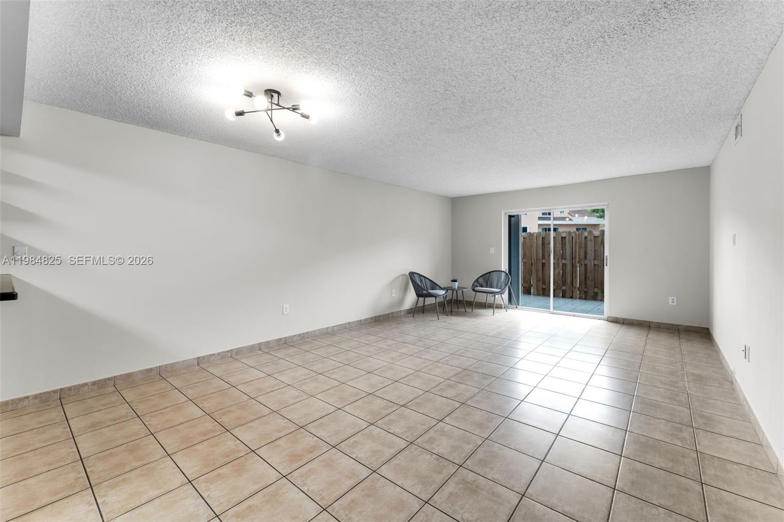 An empty room features beige tile flooring, white walls, a textured ceiling, and sliding glass doors — 14907 SW 80th St # 115, Miami FL 33193, MIAMI, FL