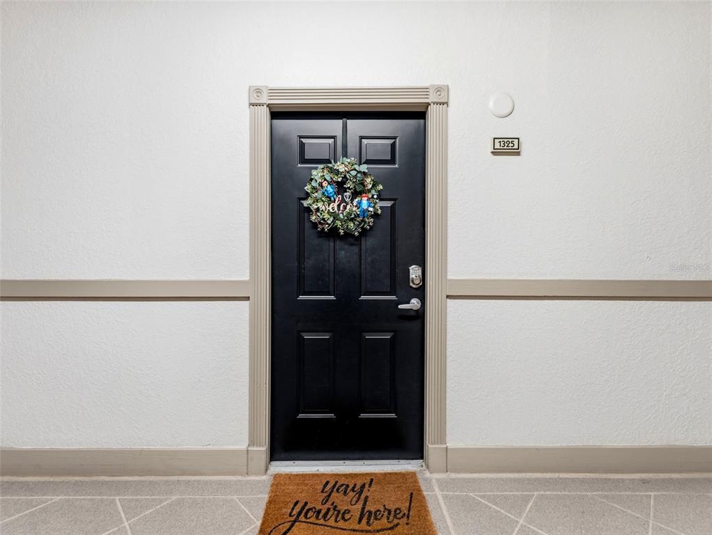A black front door with a wreath and a welcome mat is set in a wall — 501 KNIGHTS RUN AVENUE UNIT 1325, TAMPA, FL