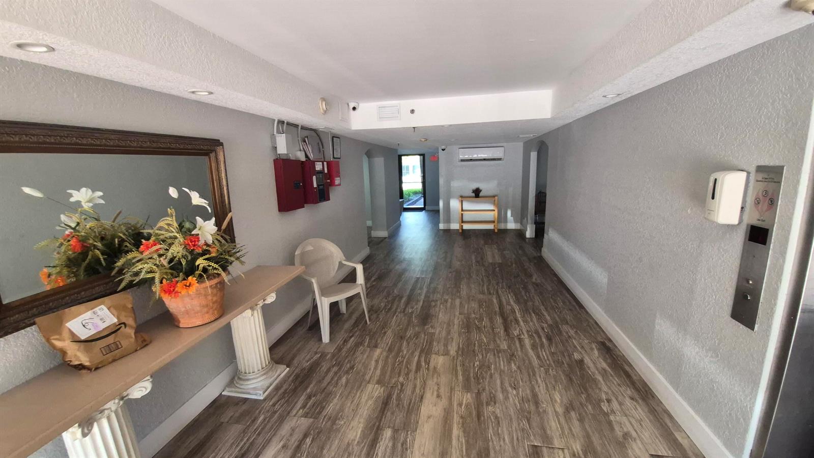 A hallway features wood-look flooring, a console table with a mirror, and an elevator panel — 450 Egret Circle # 9403, Delray Beach FL 33444, DELRAY BEACH, FL