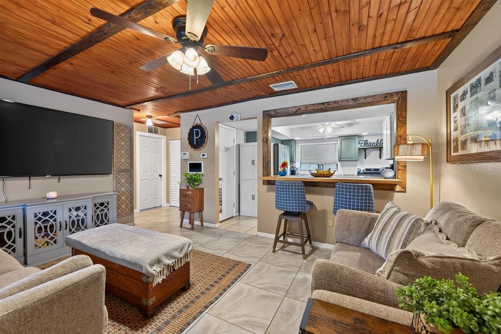 A living room features a wood-paneled ceiling, tile floors, and a pass-through to the kitchen — 10081 60TH COURT N, PINELLAS PARK, FL
