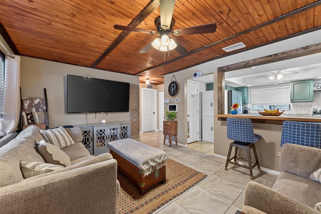 A living room with a wood-paneled ceiling, tile floors, and an open view to the kitchen — 10081 60TH COURT N, PINELLAS PARK, FL