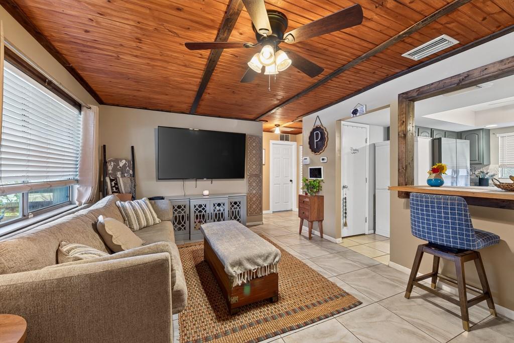A living room features a wood-paneled ceiling, tile flooring, a television, and a breakfast bar — 10081 60TH COURT N, PINELLAS PARK, FL