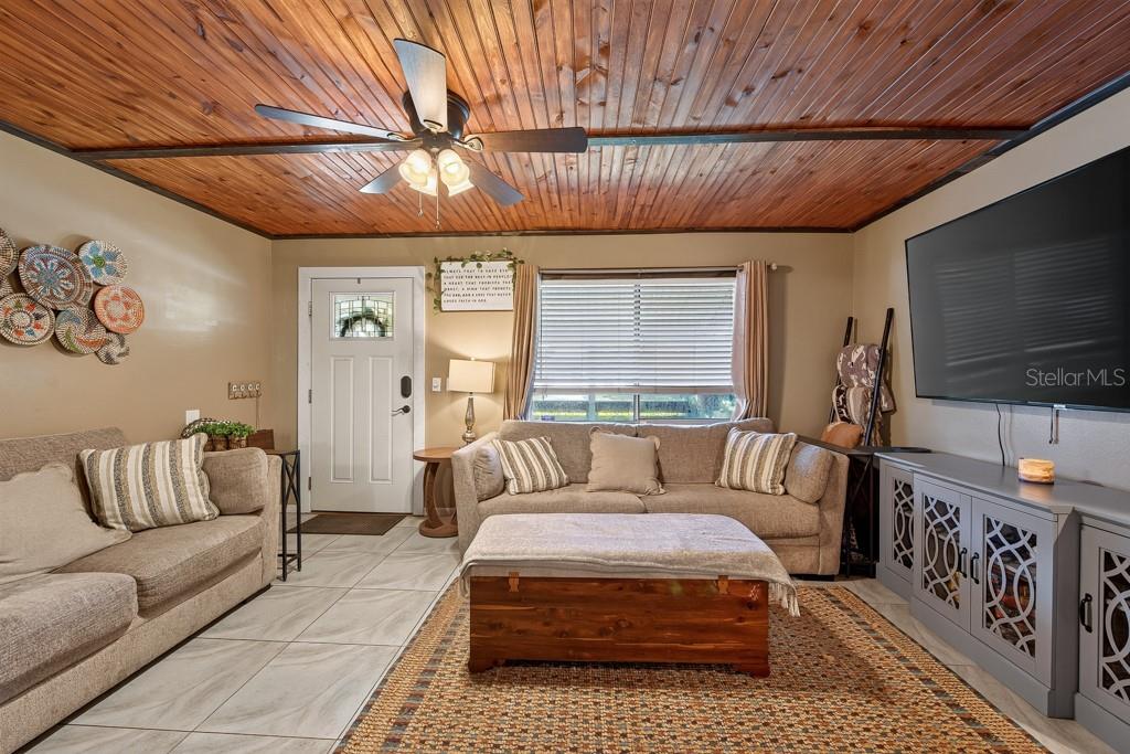 A living room features a wood-paneled ceiling, tile flooring, two sofas, and a large television — 10081 60TH COURT N, PINELLAS PARK, FL