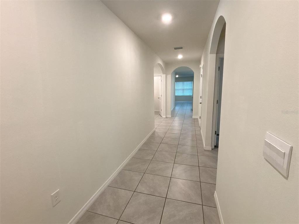 A hallway with light-colored walls and grey tiled flooring leads toward a windowed room — 500 HICKORY COURSE LOOP, OCALA, FL