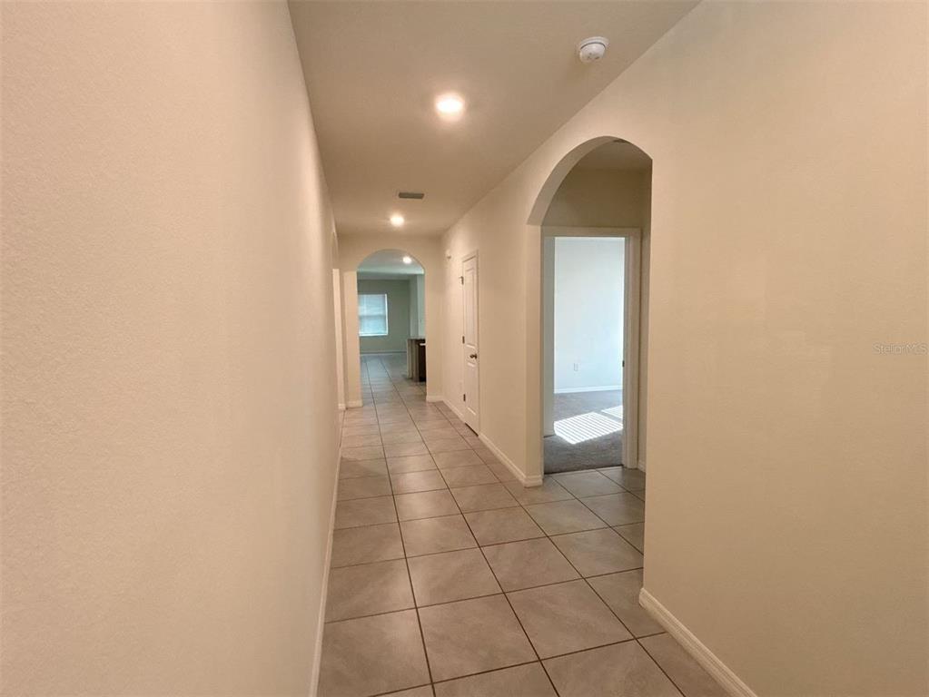 A long hallway with light-colored tile flooring leads toward an arched doorway and kitchen area — 500 HICKORY COURSE LOOP, OCALA, FL