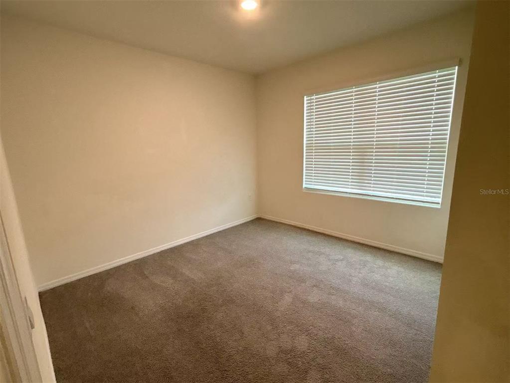 An empty bedroom features beige walls, gray carpeting, and a window with white blinds — 500 HICKORY COURSE LOOP, OCALA, FL