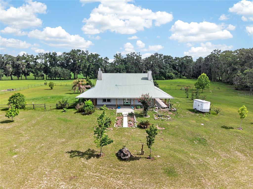 An aerial view shows a metal-roofed house surrounded by a large, grassy field and trees — 28924 SW 30TH AVENUE, NEWBERRY, FL