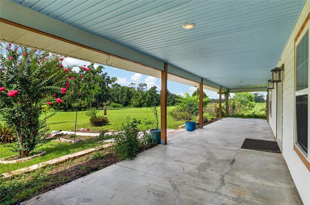 A covered concrete porch overlooks a grassy yard with trees under a blue ceiling — 28924 SW 30TH AVENUE, NEWBERRY, FL