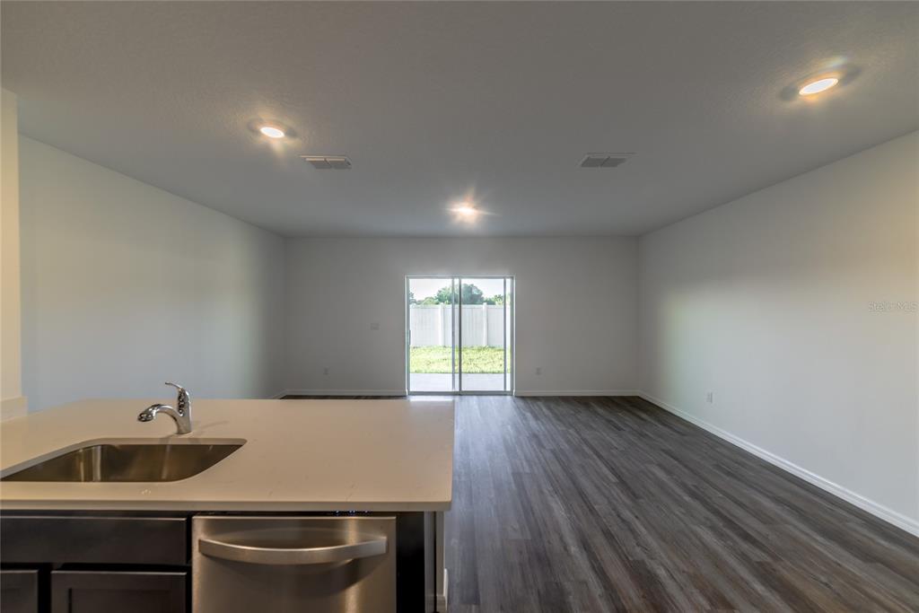 A kitchen island with a stainless steel sink overlooks an open living area with sliding doors — 17208 ENGLISH CHESTNUT WAY, LAND O LAKES, FL